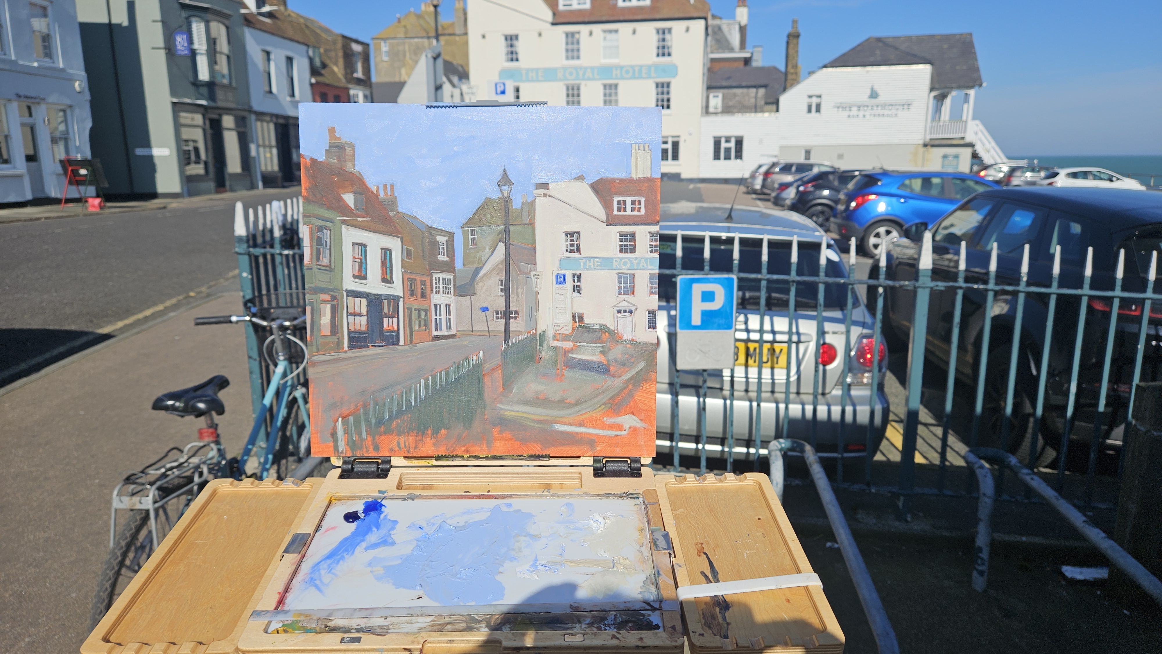 A plein air painting on an easel of a street scene by The Royal Hotel, Deal, set up on the seafront railings