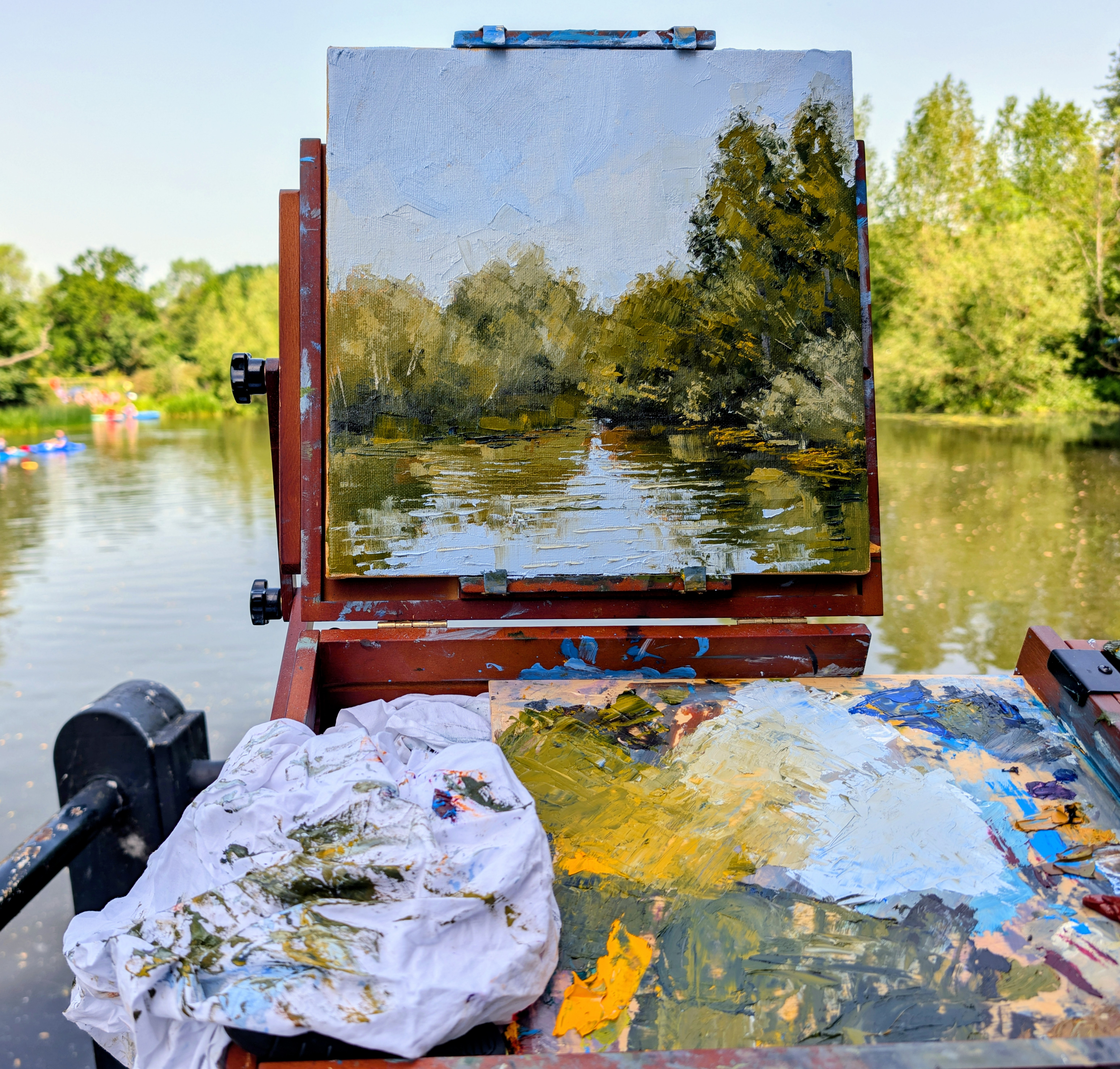 Plein air session in Dedham — painting on an easel of a tree-lined river with reflections
