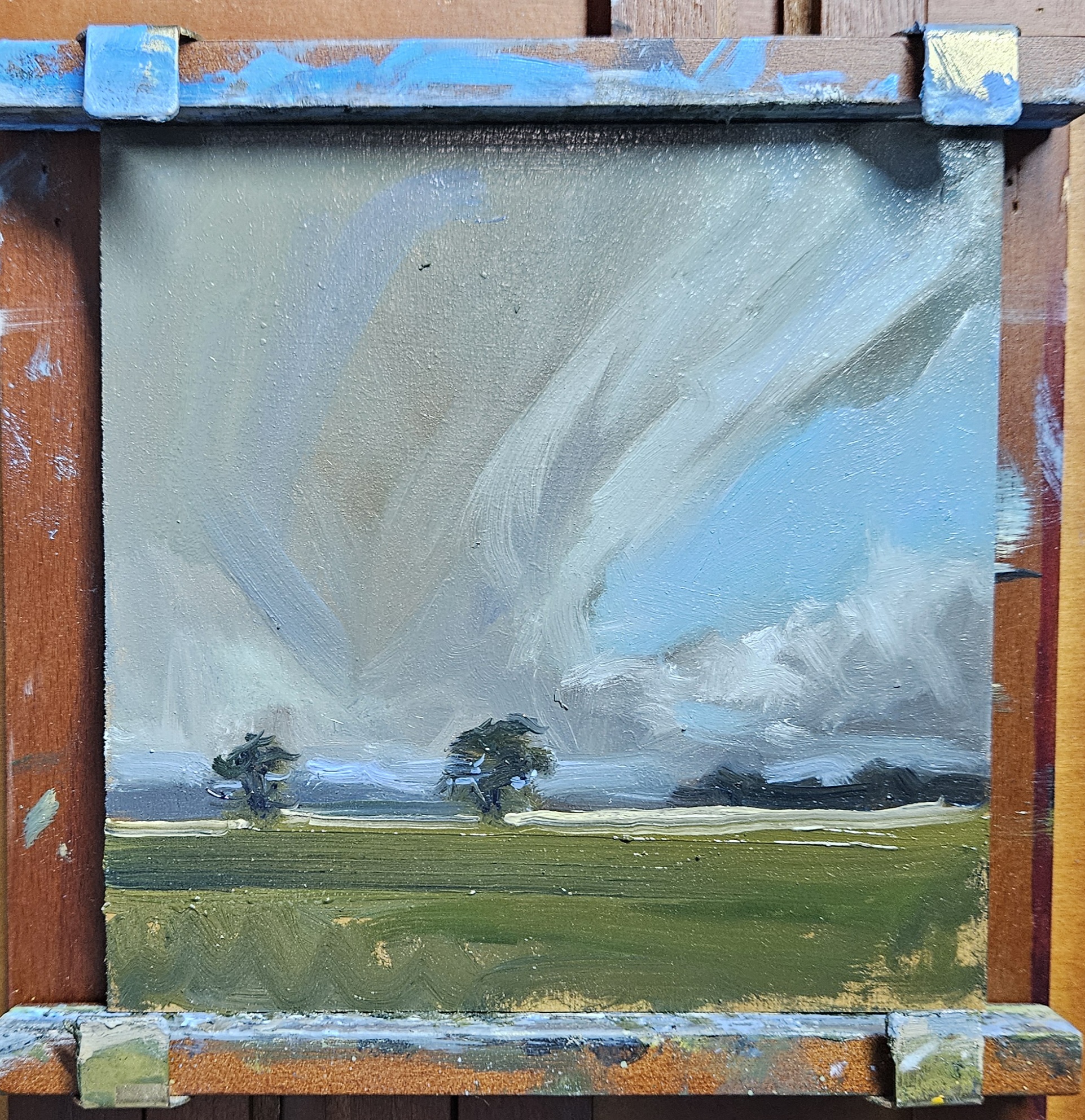 From the Back Road — oil on panel, grey rain clouds over a green field with three wind-blown trees on the horizon